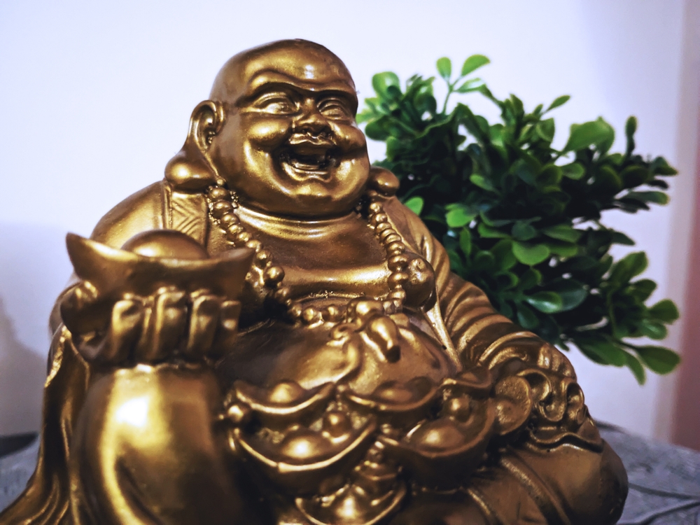 Ce aduce noroc în casă: O statuetă aurie cu Buddha care râde alături de o plantă de jad.