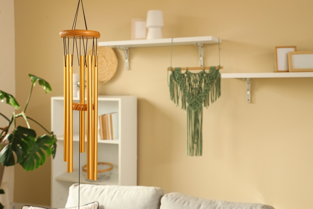 Clopoței de vânt din metal auriu atârnați îmntr-un living în stil boho cu culori calde.
