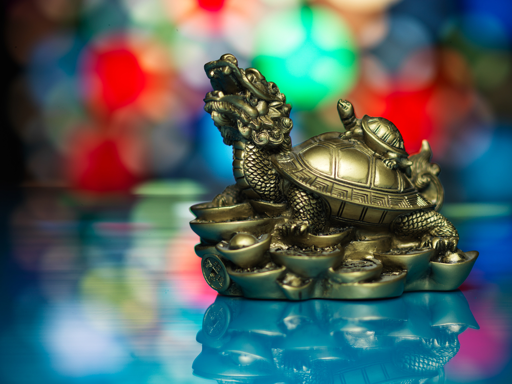 O statuetă aurie cu o țestoasă dragon din Feng Shui pe un fundal cu bookeh colorat.