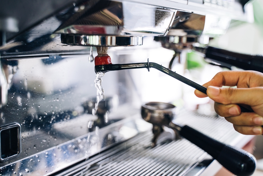 Curățare cafetieră cu oțet: o mână curăță un espressor prin pornirea unui ciclu de spălare cu apă. 