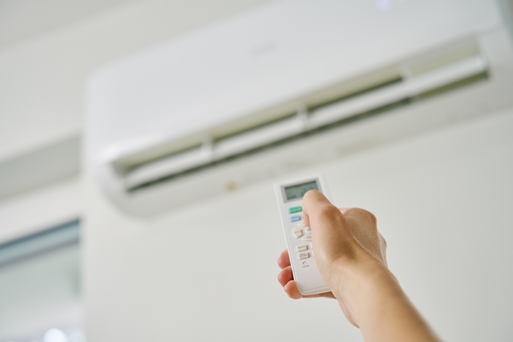 De ce nu pornește aerul condiționat: O mână îndreaptă o telecomandă albă spre un aparat de aer condiționat pe un perete alb în interior.
